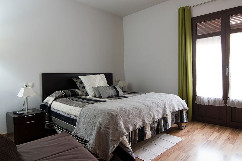 Joaquima Pellise Pedrol habitación con cama de mantas grises y cortinas verdes